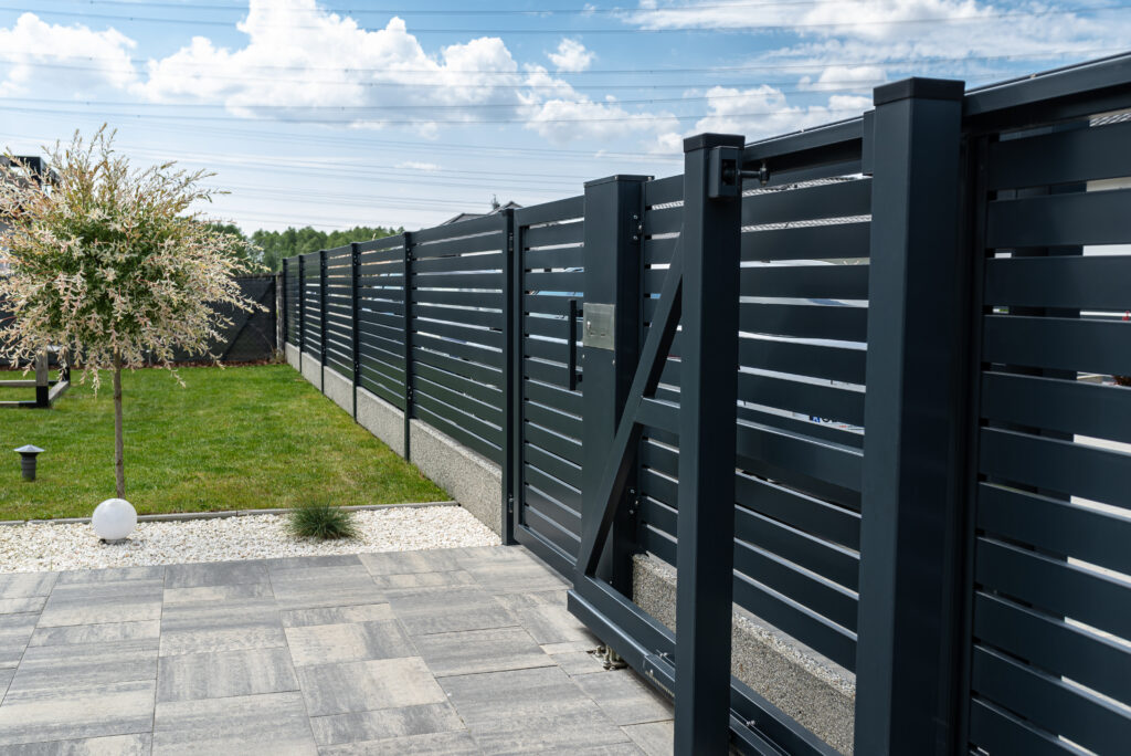 a modern panel fence in anthracite color, a visible sliding gate to the garage and a wicket with a letterbox.