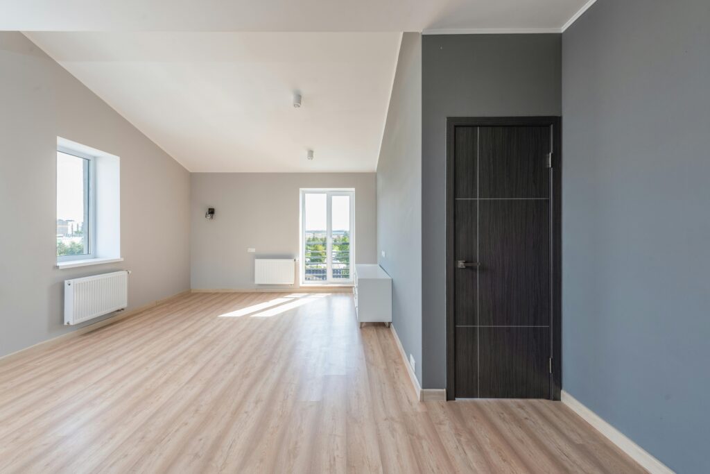 Spacious empty room with wooden flooring and large windows for ample natural light.